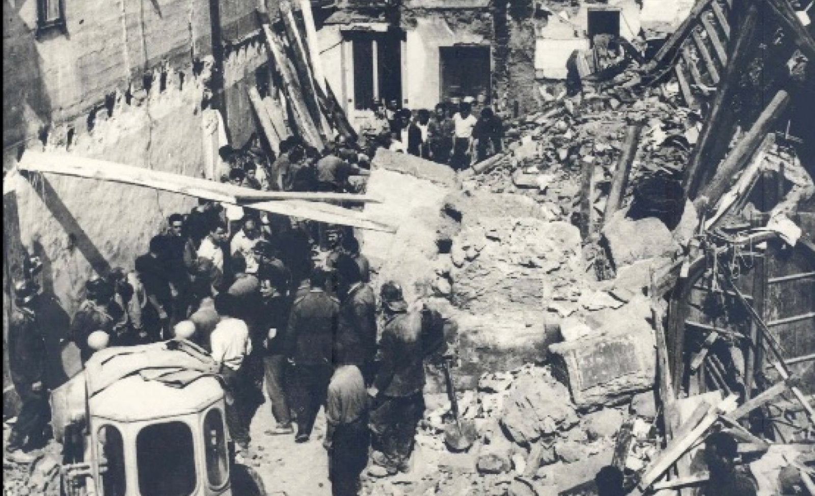 A la part inferior esquerra, un grup de bombers davant un edifici enfonsat per la riuada.