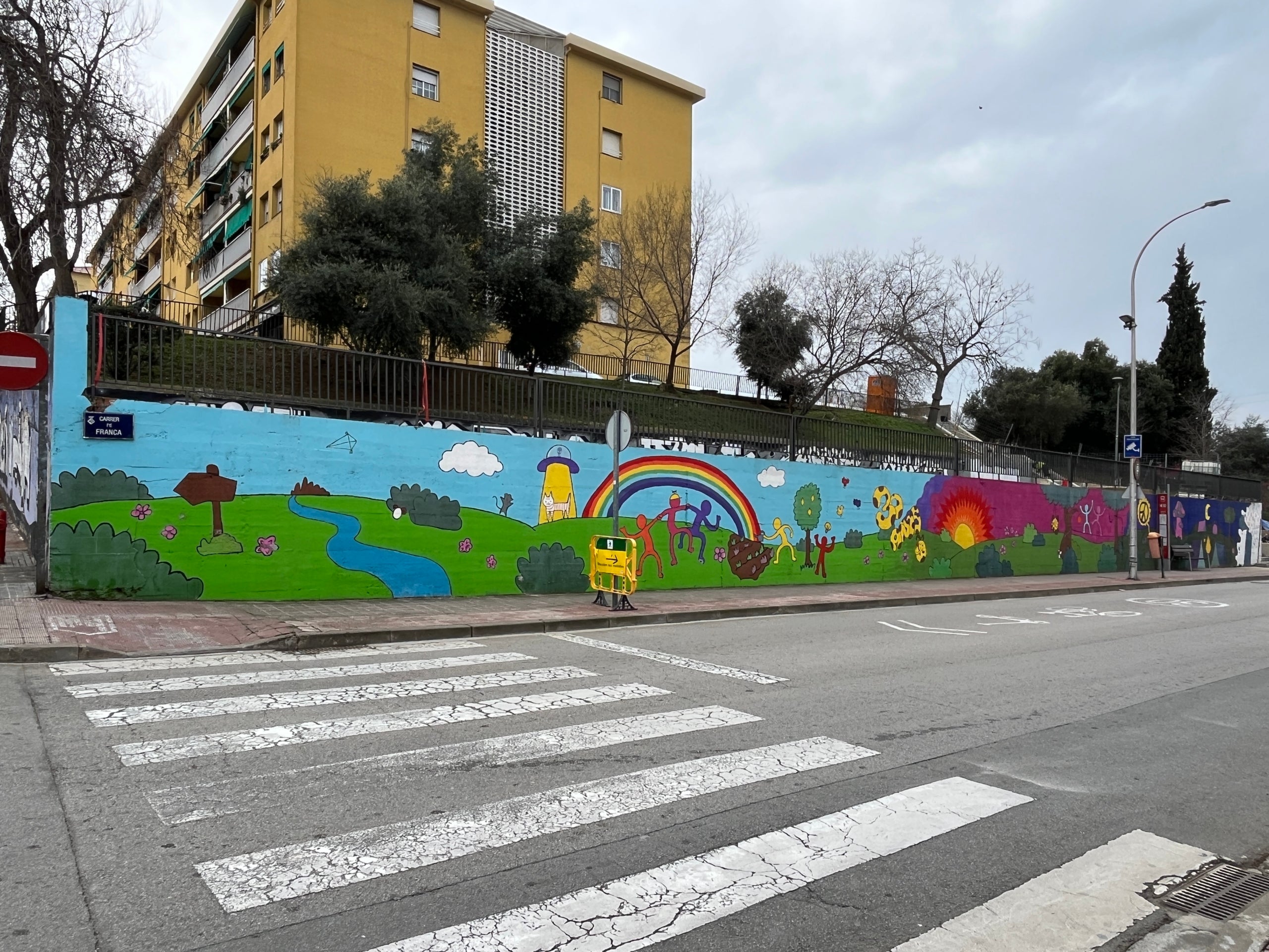 Echamos un vistazo al Museo Vivo en Can Parellada. En los últimos meses, se ha llevado a cabo un proyecto sociocultural impulsado desde la AV Can Parellada por la Unidad que ha tenido como objetivo dignificar el espacio público del barrio. Con la colaboración de Juan Manuel Pacheco, se ha introducido un toque de color y creatividad en diferentes paredes y muros. Escenas cotidianas, mensajes de civismo, colores, formas… todo para crear un ambiente agradable. También han participado los jóvenes y monitores del esplai de Can Parellada | Lucia Rivera