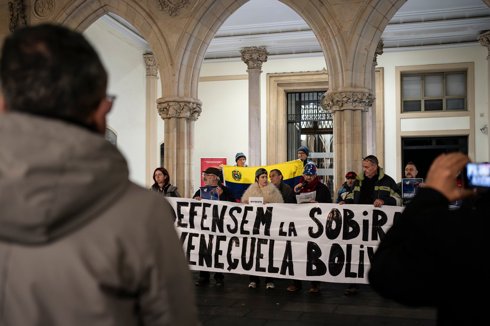Acte de protesta aquest divendres, dia 16 de gener, davant de l’Ajuntament de Terrassa contra la intervenció militar dels EUA a la República Bolivariana de Veneçuela, del passat 3 de gener. La concentració ha estat convocada pel Comitè Bolivarià de Terrassa ha demanat a la Unió Europea mediar per una resolució diplomàtica i pacífica dels conflictes, “trencant amb el vassallatge i la dependència dels Estats Units”, així com ha exigit l’alliberament “immediat” del president Nicolás Maduro i de la diputada Cilia Flores. 