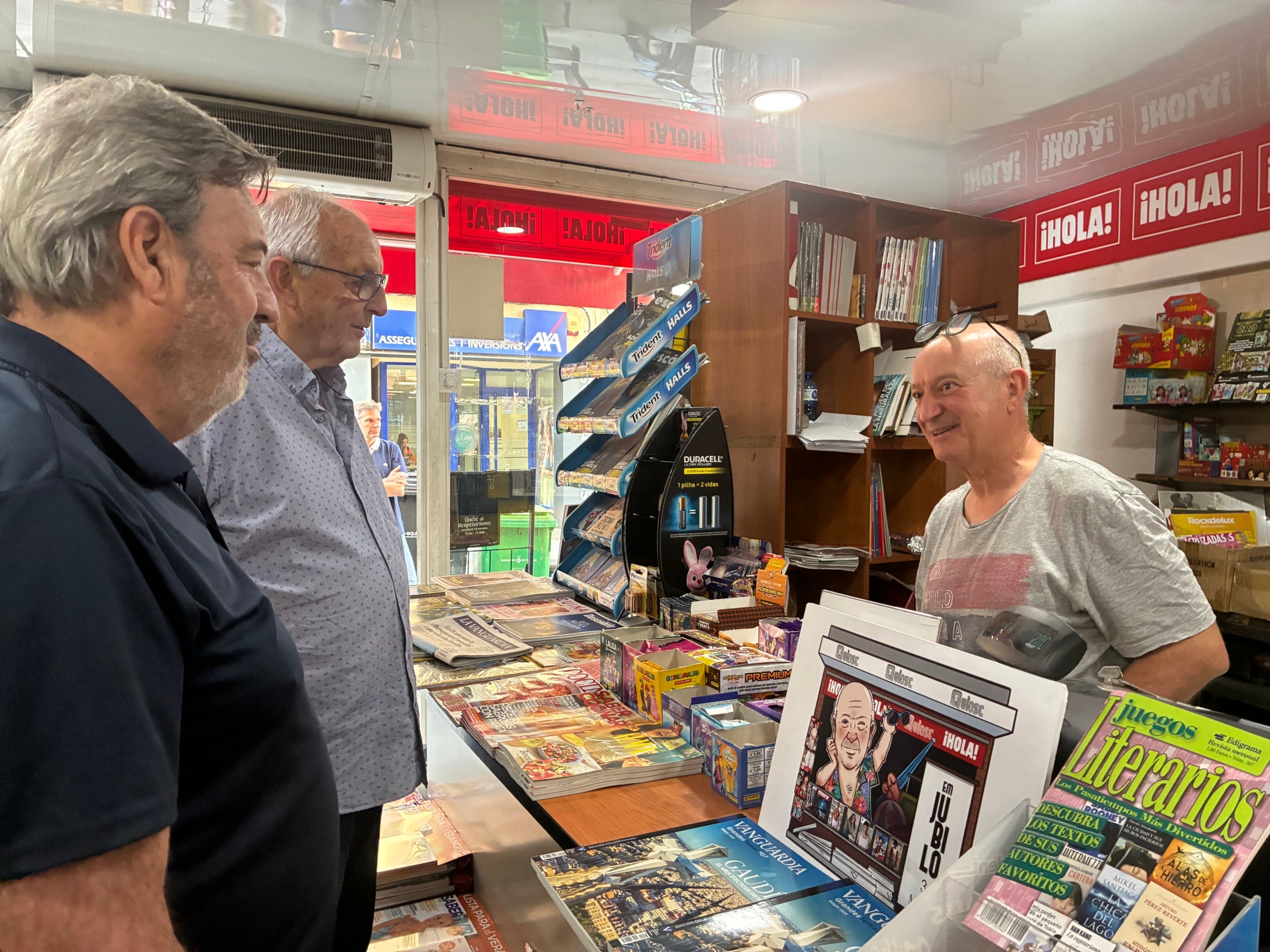 Joan Garcia, darrera el mostrador, aquest dilluns saludant els seus últims clients abans de tancar El Quiosc del carrer Nou de Sant Pere on hi ha treballat 52 anys | Vicenç Batalla