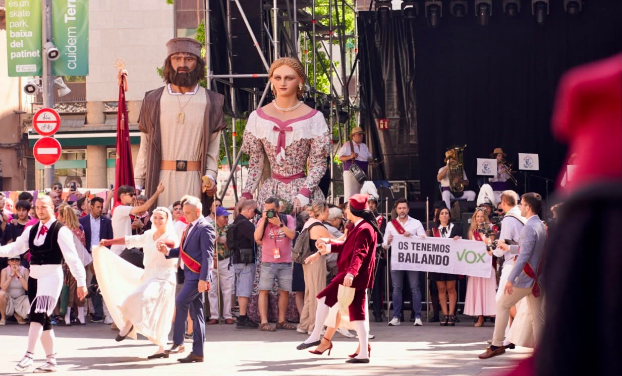 Moment en què L'Esbart Egarenc treu a ballar els regidors a la plaça Vella per Festa Major però tornant a deixar de banda els de Vox, que despleguen una pancarta | Mireia Comas